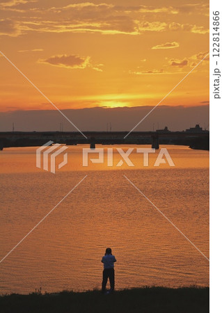 夕焼けの川を眺める男性 122814866