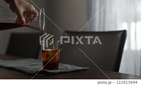 man pours fresh coffee over ice rock in tumbler glass on wood table 122815694