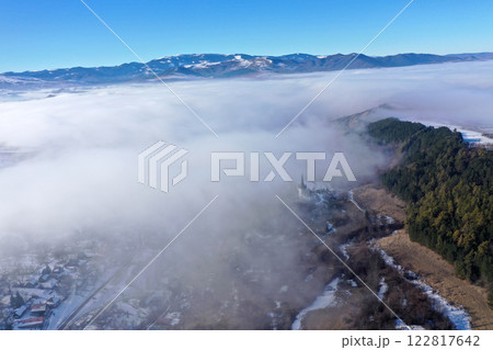 Aerial view of foggy misty mountain village and church tower at winter 122817642