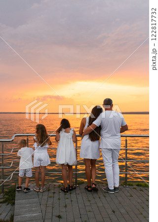Happy family of five is standing on pier overlooking the ocean and enjoying the view and taking in the peaceful atmosphere 122817732