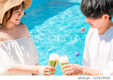 バカンス・リゾートホテルのプールサイドでビールグラスで乾杯するカップル バカンス・リゾートホテルのプールサイドでビールグラスで乾杯するカップル 122819426