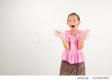 Portrait Thailand kid girl smiling traditional Thai dress costume raises fists in celebration of her success, studio isolated white background, kindergarten child saying yes with excitement winning 122820487