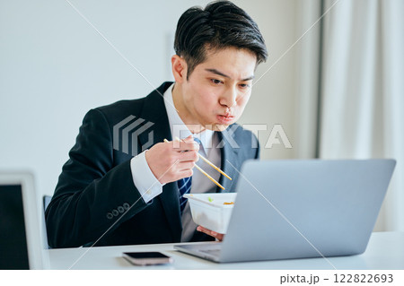 カップ焼きそばを食べながら仕事をする20代の若い男性 カップ焼きそばを食べながら仕事をする20代の若い男性 122822693