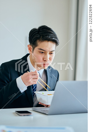 カップ焼きそばを食べながら仕事をする20代の若い男性 122822694