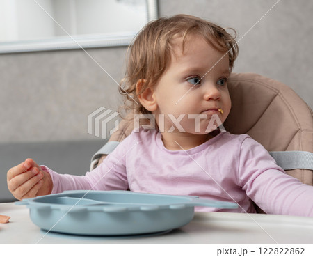 A curious toddler distracted during mealtime, observing surroundings with food in mouth A curious toddler distracted during mealtime, observing surroundings with food in mouth 122822862
