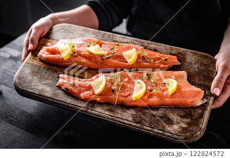 Girl hands holding fresh trout salmon filet with herbs and lemons. Woman cooking omega orange fish with rosemary for healthy nutrition Girl hands holding fresh trout salmon filet with herbs and lemons. Woman cooking omega orange fish with rosemary for healthy nutrition 122824572