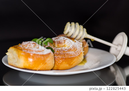 Baked goods. Sweet buns with cottage cheese filling and honey in a plate isolated on a black background 122825443
