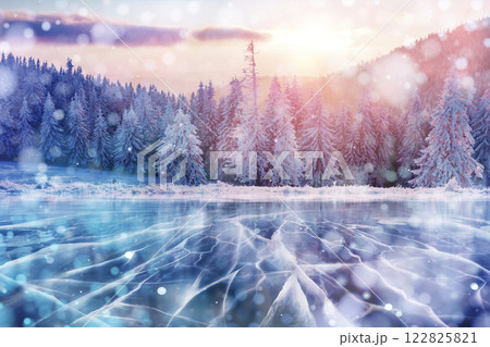 Blue ice and cracks on the surface of the ice. Frozen lake in winter mountains. It is snowing. The hills of pines. Winter. Carpathian Ukraine Europe 122825821