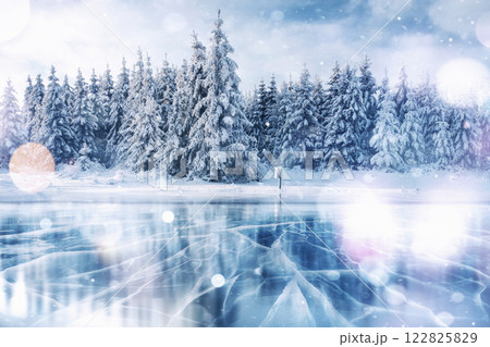 Blue ice and cracks on the surface of the ice. Frozen lake in winter mountains. It is snowing. The hills of pines. Winter. Carpathian Ukraine Europe 122825829
