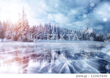 Blue ice and cracks on the surface of the ice. Frozen lake in winter mountains. It is snowing. The hills of pines. Winter. Carpathian Ukraine Europe 122825830