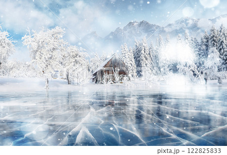 Blue ice and cracks on the surface of the ice. Frozen lake in winter mountains. It is snowing. The hills of pines. Winter. Carpathian Ukraine Europe 122825833