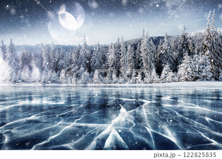 Blue ice and cracks on the surface of the ice. Frozen lake in winter mountains. It is snowing. The hills of pines. Winter. Carpathian Ukraine Europe Blue ice and cracks on the surface of the ice. Frozen lake in winter mountains. It is snowing. The hills of pines. Winter. Carpathian Ukraine Europe 122825835