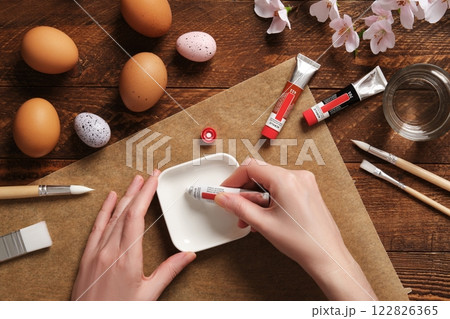 Women's hands squeeze paint out of a tube. Preparation for the celebration of Easter. Painting Easter eggs with acrylic pigment dyes in tubes. Women's hands squeeze paint out of a tube. Preparation for the celebration of Easter. Painting Easter eggs with acrylic pigment dyes in tubes. 122826365