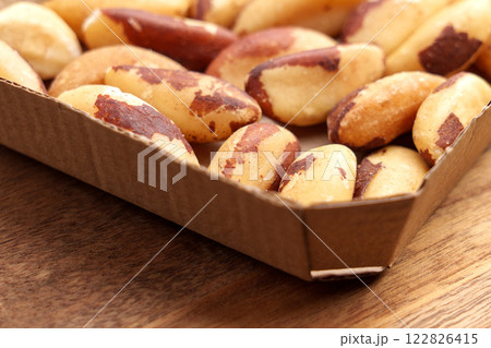 Peeled Brazil nuts in a compostable cardboard container on a wooden table. Sustainable snack with selenium nutrients and healthy fats. Close-up Peeled Brazil nuts in a compostable cardboard container on a wooden table. Sustainable snack with selenium nutrients and healthy fats. Close-up 122826415