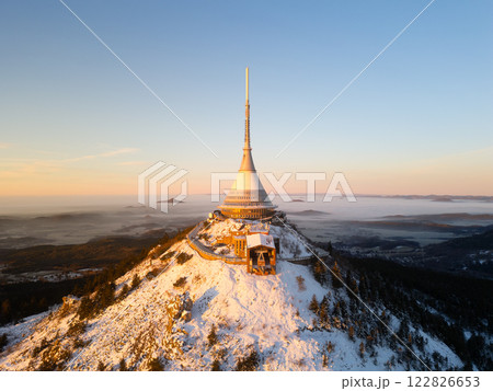 Jested Mountain showcases a breathtaking sunrise, illuminating the snowy landscape and its distinctive tower. The cold winter air adds a serene atmosphere to the scene. Jested Mountain showcases a breathtaking sunrise, illuminating the snowy landscape and its distinctive tower. The cold winter air adds a serene atmosphere to the scene. 122826653
