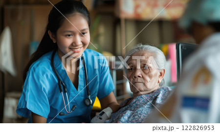 young caregiver in blue uniform smiles while assisting elderly woman 122826953