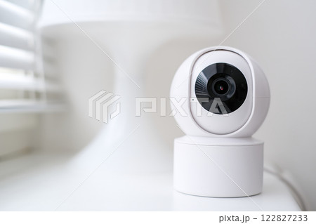 Smart home security camera on a white table near a window. Smart home security camera on a white table near a window. 122827233