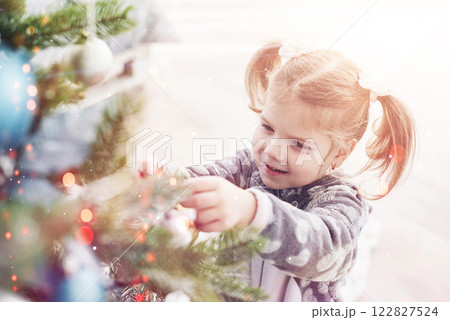 Merry Christmas and Happy Holidays! Young girl helping decorating the Christmas tree, holding some Christmas baubles in her hand 122827524