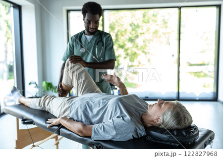 Female patient lying on a couch while male doctor working on her legs stretching Female patient lying on a couch while male doctor working on her legs stretching 122827968