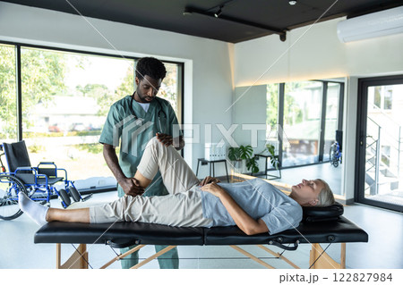 Female patient lying on a couch while male doctor working on her legs stretching Female patient lying on a couch while male doctor working on her legs stretching 122827984