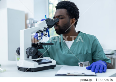 Male scientist looking under microscope inspecting petri dish 122828010