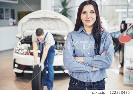 Mechanic holding a tire tire at the repair garage. The client woman waits for the job Mechanic holding a tire tire at the repair garage. The client woman waits for the job 122828480