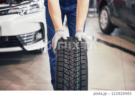 Closeup of mechanic hands pushing a black tire in the workshop Closeup of mechanic hands pushing a black tire in the workshop 122828483