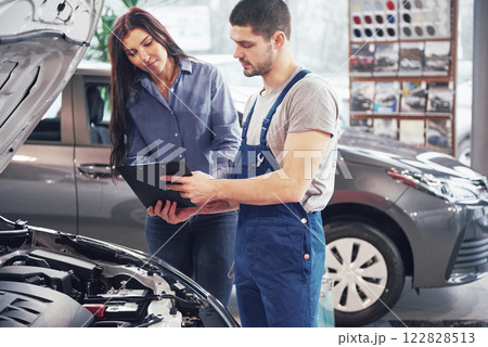 A man mechanic and woman customer discussing repairs done to her vehicle A man mechanic and woman customer discussing repairs done to her vehicle 122828513