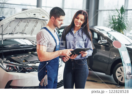 A man mechanic and woman customer discussing repairs done to her vehicle A man mechanic and woman customer discussing repairs done to her vehicle 122828528