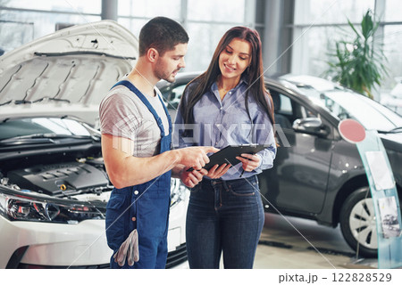A man mechanic and woman customer discussing repairs done to her vehicle A man mechanic and woman customer discussing repairs done to her vehicle 122828529