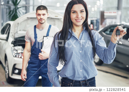 A young woman takes a car from the car service center. She is happy because the work is done perfectly 122828541