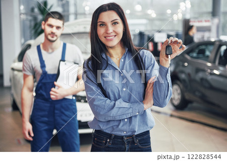 A young woman takes a car from the car service center. She is happy because the work is done perfectly A young woman takes a car from the car service center. She is happy because the work is done perfectly 122828544