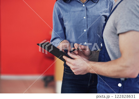 Beautiful young woman is talking to handsome car mechanic while repair a car in dealership 122828631