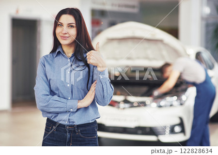 The woman approves the work done by the client. The mechanic works under the hood of the car 122828634