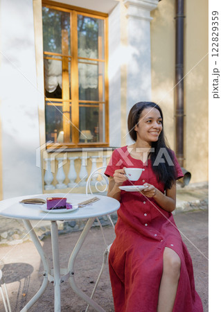young African American woman in burgundy dress drinks tea in park in coffee shop 122829359