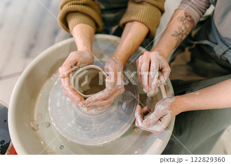 Hands-on learning, senior woman mastering pottery techniques using rotating wheel Mentor teaches pottery fundamentals, demonstrating sculpting skills on an electric wheel Hands-on learning, senior woman mastering pottery techniques using rotating wheel Mentor teaches pottery fundamentals, demonstrating sculpting skills on an electric wheel 122829360