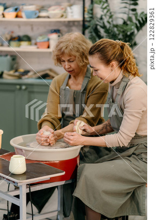 Hands-on learning, senior woman mastering pottery techniques using rotating wheel Mentor teaches pottery fundamentals, demonstrating sculpting skills on an electric wheel 122829361