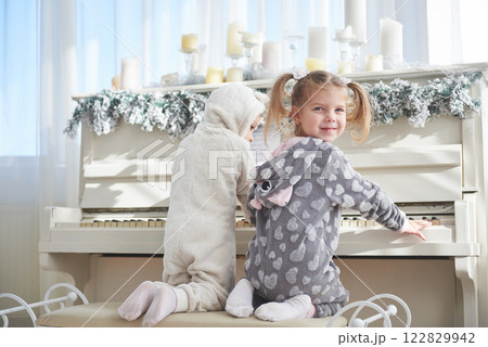 Two happy little girls in pajamas play the piano on Christmas day 122829942