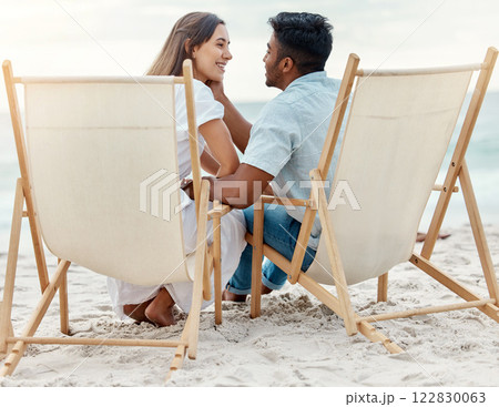 Couple, love and beach vacation of summer holiday with interracial lovers sharing a romantic moment while sitting on chairs in the sand. Happy and young man and woman on tropical honeymoon together Couple, love and beach vacation of summer holiday with interracial lovers sharing a romantic moment while sitting on chairs in the sand. Happy and young man and woman on tropical honeymoon together 122830063