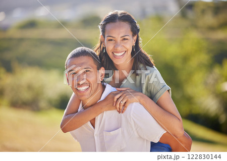 Portrait, piggyback and happy couple in nature on a romantic date, vacation or walk in green garden. Love, care and smile of a husband and wife bonding in an outdoor park while on a summer holiday. 122830144