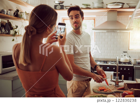 Cooking man sticking out tongue to make silly, goofy and funny face to pose for a photo while making food in the kitchen at home. Crazy, fun and happy couple enjoying a playful moment while bonding 122830238