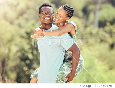 Love, date and outdoor couple in park or romantic nature outing for healthy, green lifestyle with trees, bokeh and lens flare. Happy, wellness black people and caring man giving woman piggyback ride 122830476