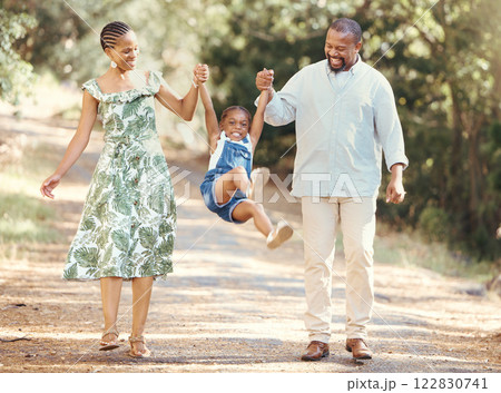 Happy parents swing girl at their hands in the forest during a walk in nature. Cheerful kid having fun while bonding with mother and father on family summer vacation or outing together in the woods Happy parents swing girl at their hands in the forest during a walk in nature. Cheerful kid having fun while bonding with mother and father on family summer vacation or outing together in the woods 122830741