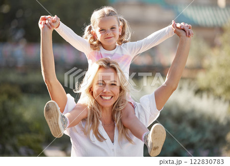 Happy mother playing with daughter on her shoulders in their backyard on a sunny day. Energetic woman play and having fun with her girl. Family bonding and laughing together on the weekend 122830783