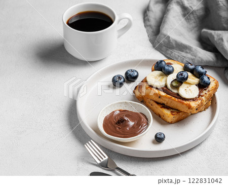 Toasted bread with chocolate cream, blueberries and banana on a plate on a light background Toasted bread with chocolate cream, blueberries and banana on a plate on a light background 122831042
