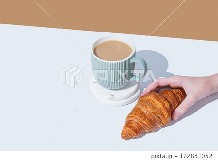 Hand holding fresh croissant on white broun background and cup of coffee with milk. Hand holding fresh croissant on white broun background and cup of coffee with milk. 122831052