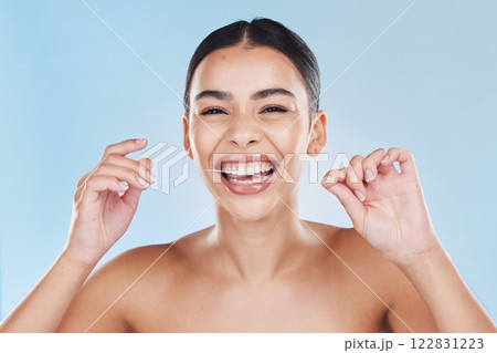 Beauty, teeth and skincare of a woman in dental floss isolated against a blue studio background. Portrait of attractive female flossing for healthy mouth care, tooth and gum hygiene with a big smile. 122831223