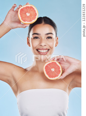 Wellness, health and beauty with woman and grapefruit with a smile against a blue background studio. Skincare, nutrition and confident portrait of a young wellbeing female holding fruit 122831229