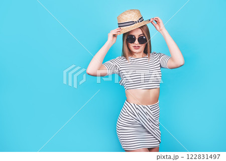 Attractive girl in a white and black stripes, hat, sunglasses, emotionally opened mouth on a bright blue background with a perfect body. Isolated. Studio shot 122831497