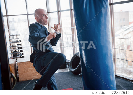 An angry bald businessman beats a boxing pear in the gym. concept of anger management An angry bald businessman beats a boxing pear in the gym. concept of anger management 122832630